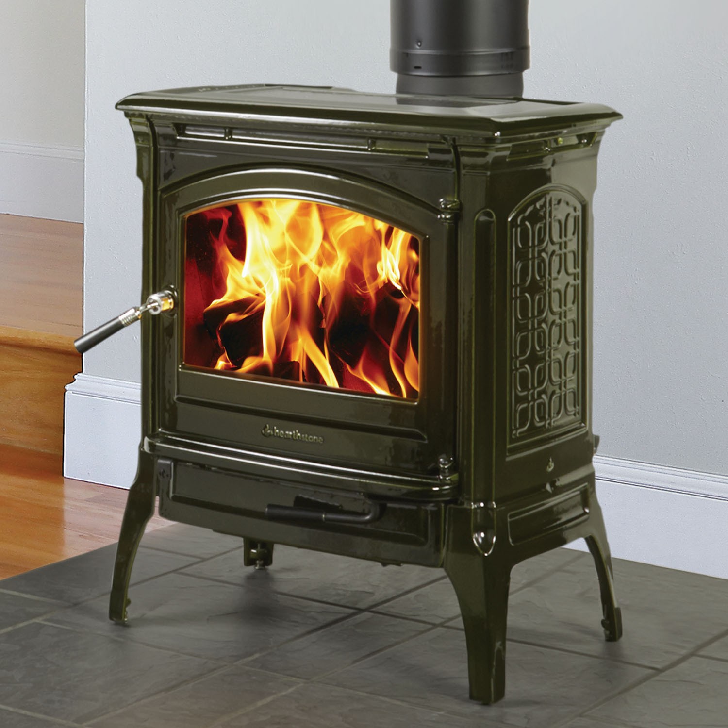 Traditional Cast Iron Stove with design on the side glass front with handle on tile flooring and gray wall in the background.