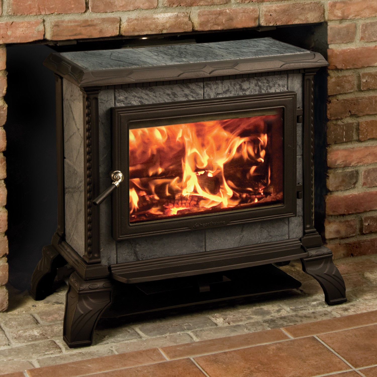 Homestead Freestanding 8570F Wood Stove made of black iron and granite with brick background and hearth.