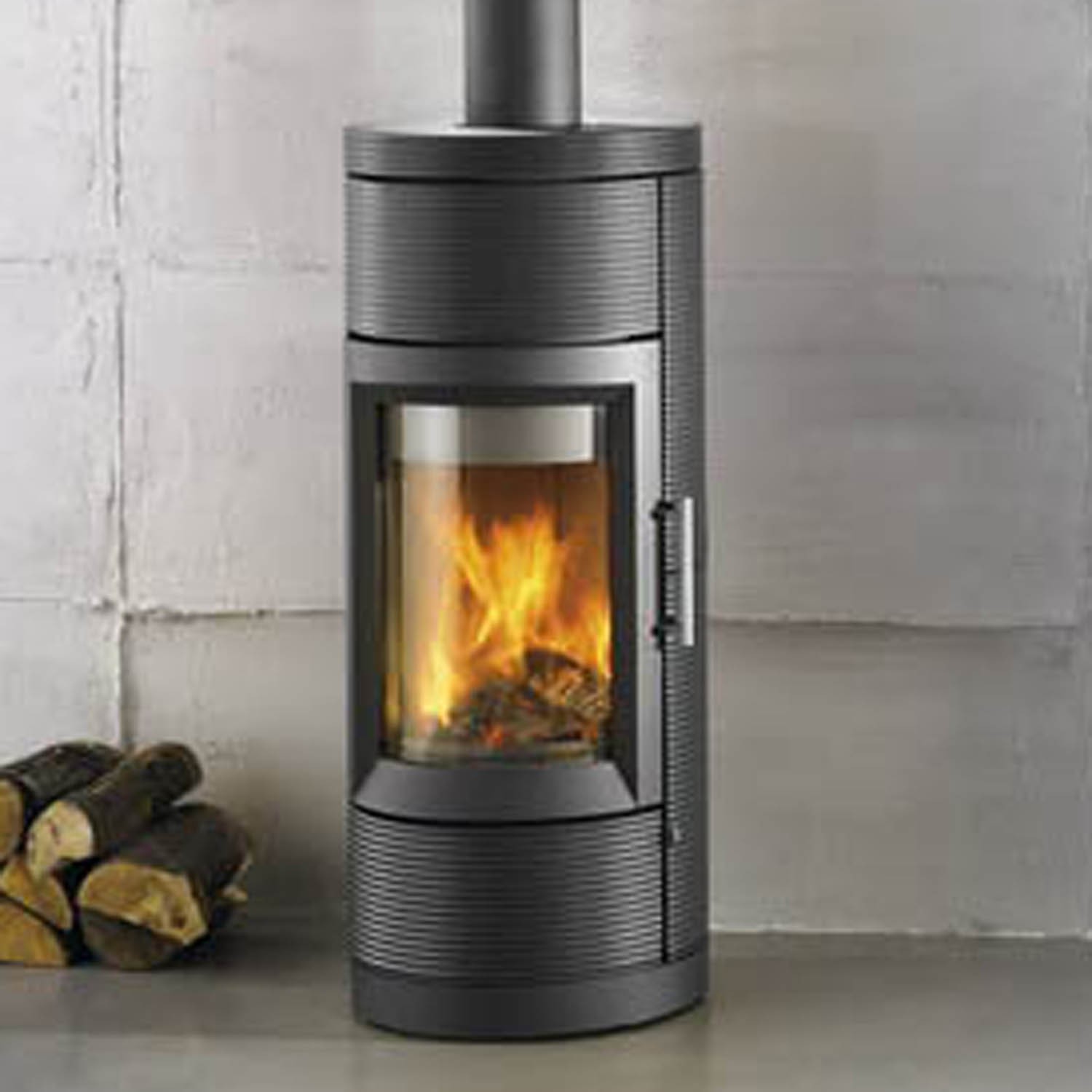 Lima 8150 Wood Stove in black, round, wood to the left, concrete flooring and concrete wall in the background.