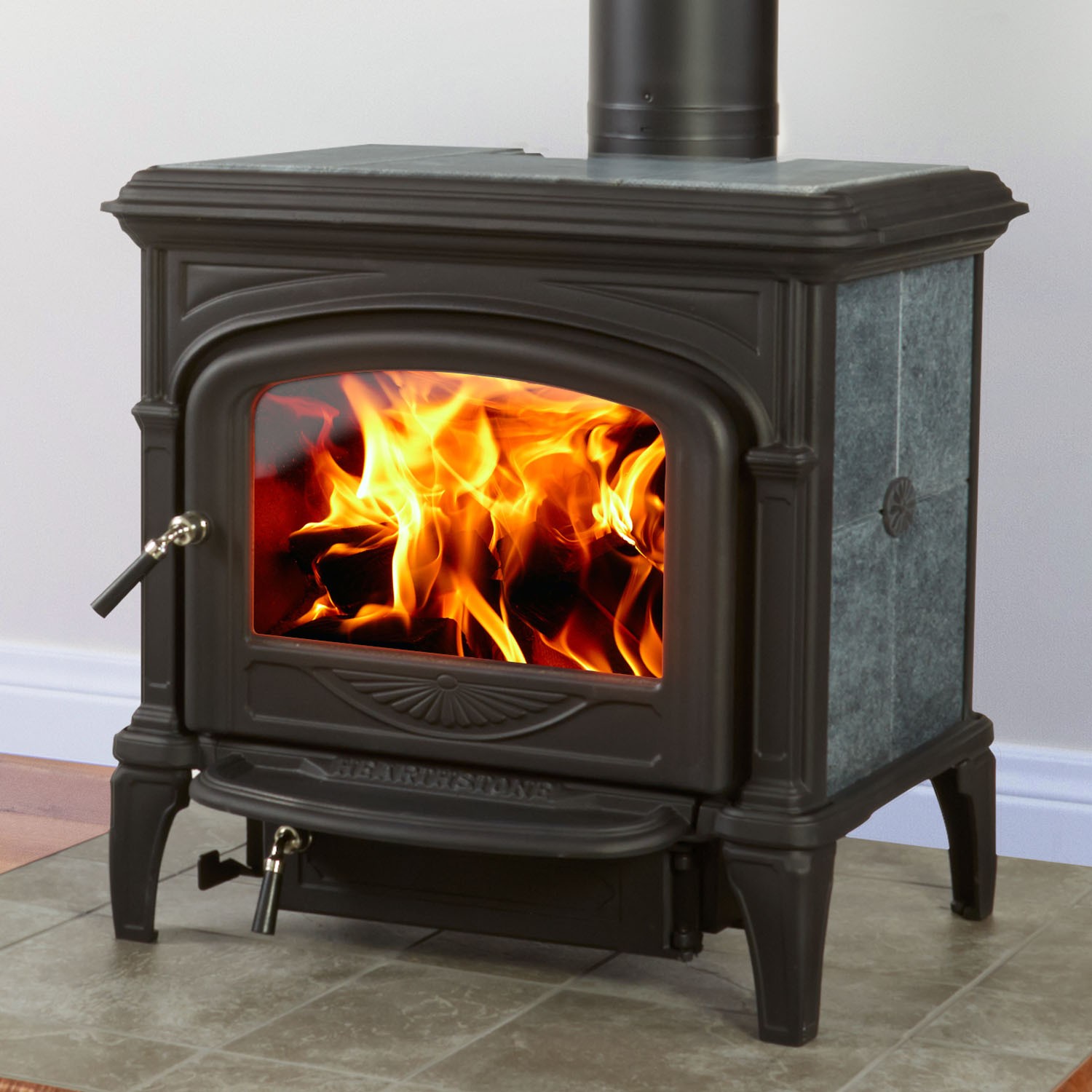 Phoenix 8612 Wood Stove - Iron and granite tile with door and handle.  Large flames going.  The flooring is sage green tile with a gray wall in the background.