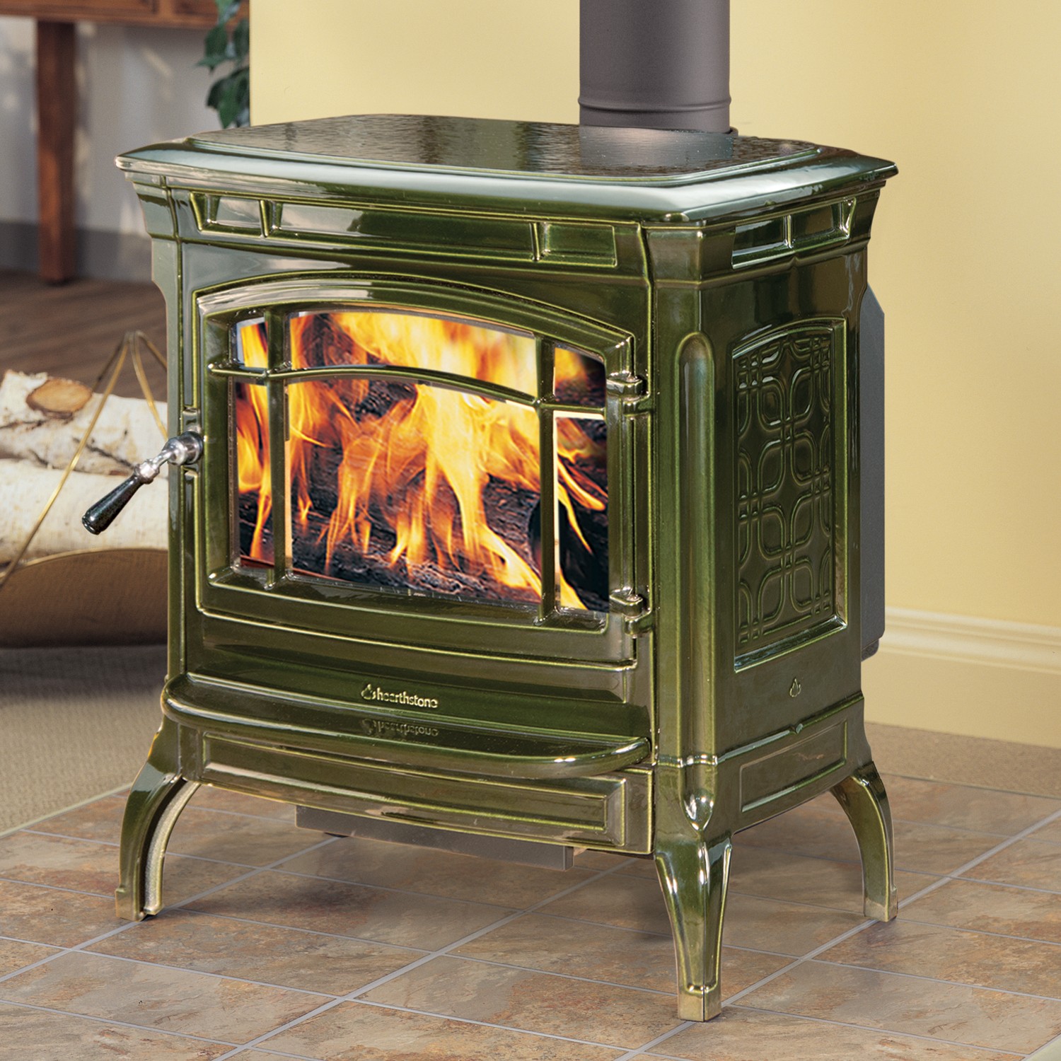 Shelburne 8371 Wood Stove in green cast iron with glass door and handle with designs o the side.  Cream colored wall in the background and terra cotta tile on the hearth.