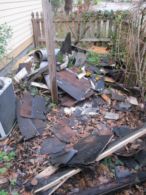 chimney and roofing debris all over the ground with a picket fence in the background.
