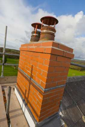 Large Brown Brick Chimney with two vents on top sitting on a roof of a home