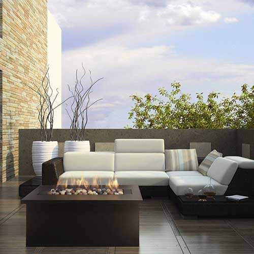 Outdoor gas fireplace with corner sofa and plants with blue sky.