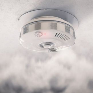 white smoke detector with a red light surrounded by smoke