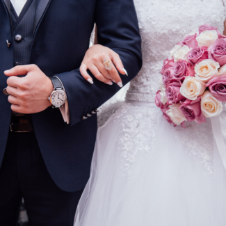 a bride and grooms arms linked with pink flowers