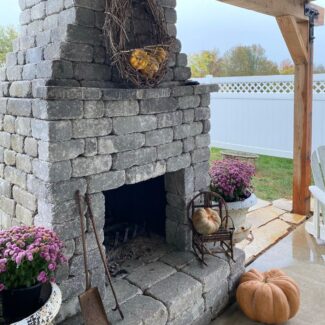 a gray brick outdoor fireplace with pumpkin decor around it