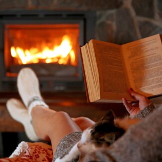 a person reading and relaxing by a fireplace with a cat on their lap