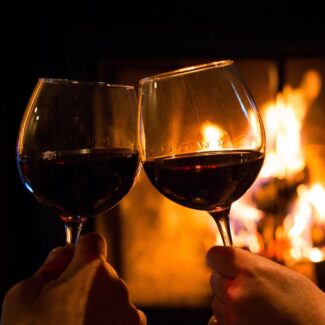 two wine glasses clinking in front of a fireplace
